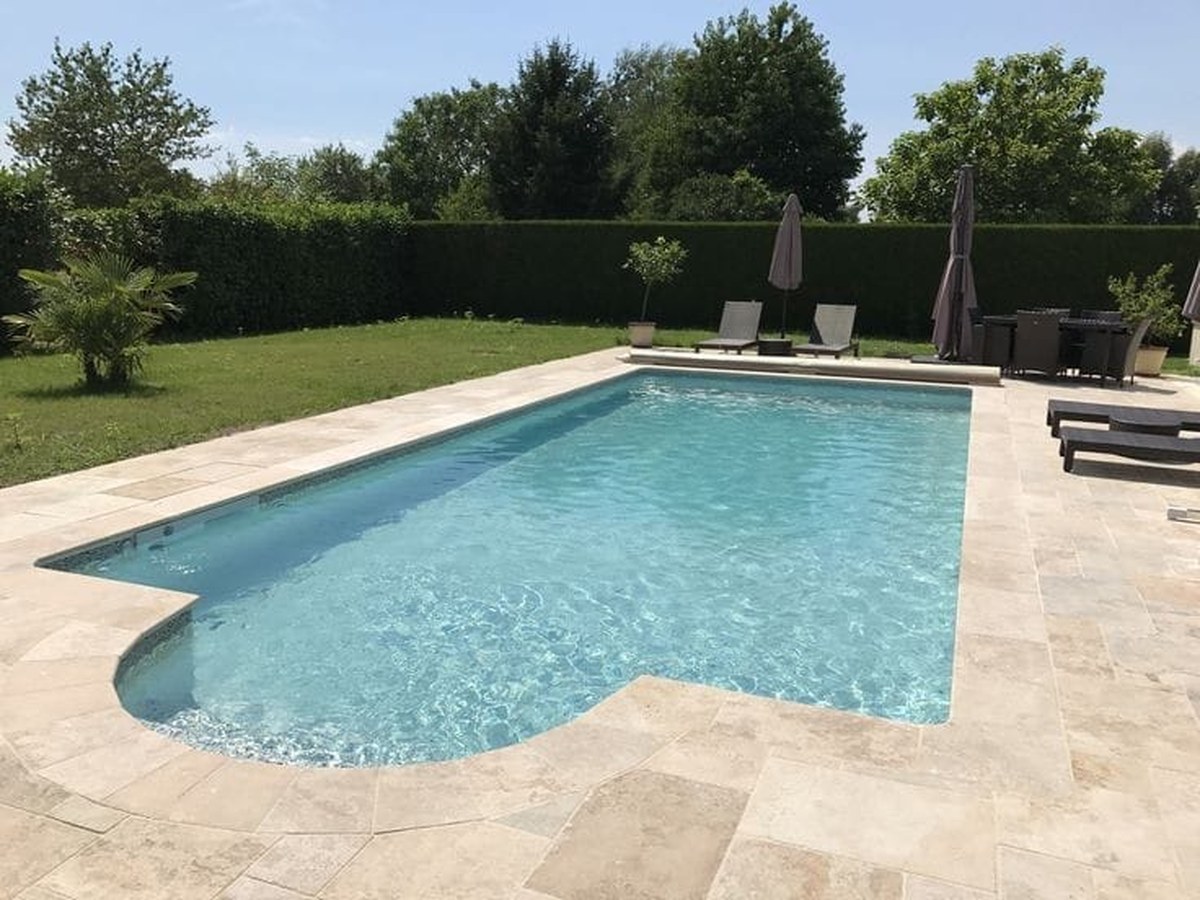 Deck de piscina revestido em travertino na paginação francesa, com quatro tamanhos de peça intercalados e junta aparente