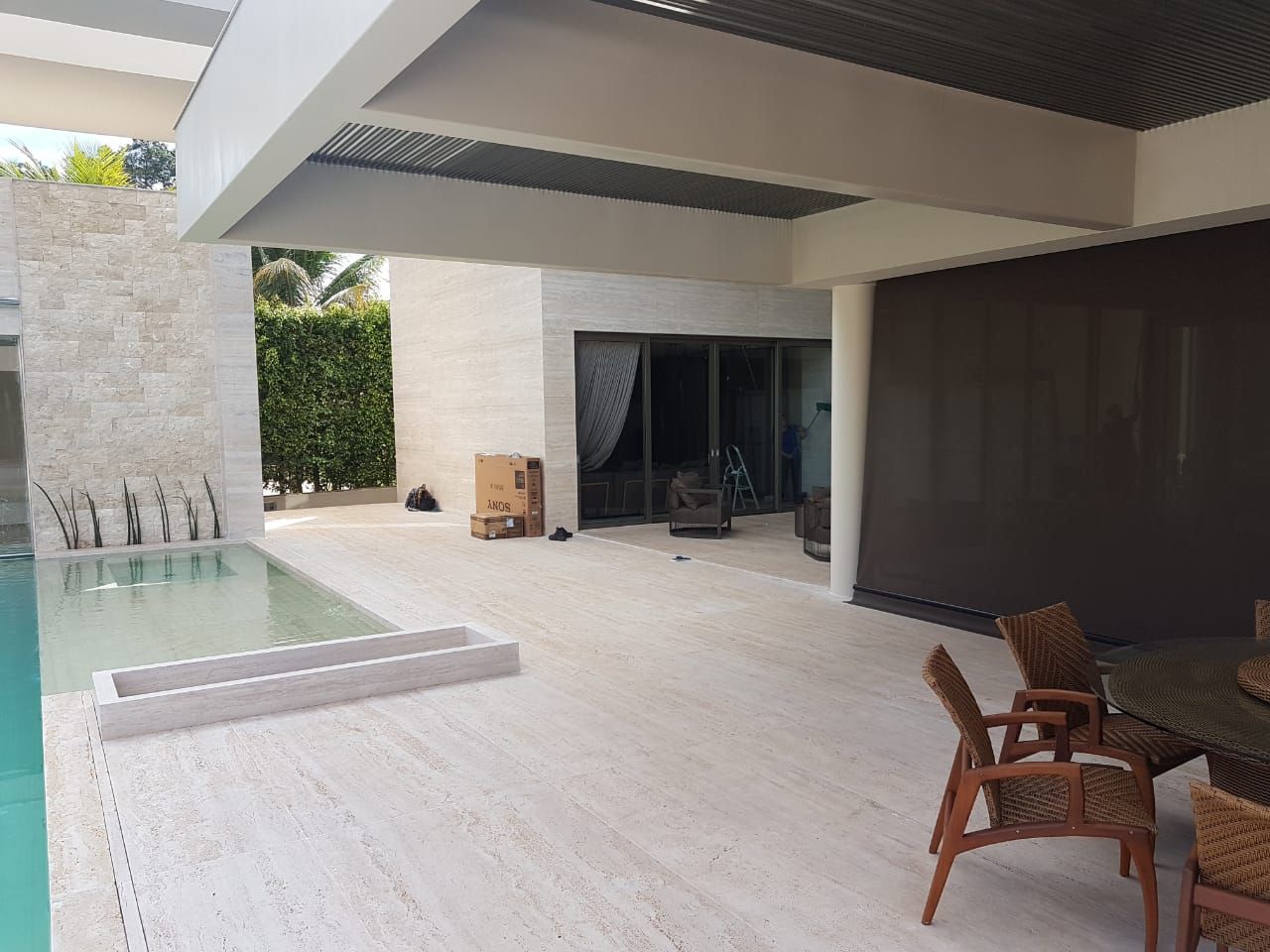 Varanda coberta ao lado da piscina, com piso contínuo de travertino claro seguindo do interior para a borda
