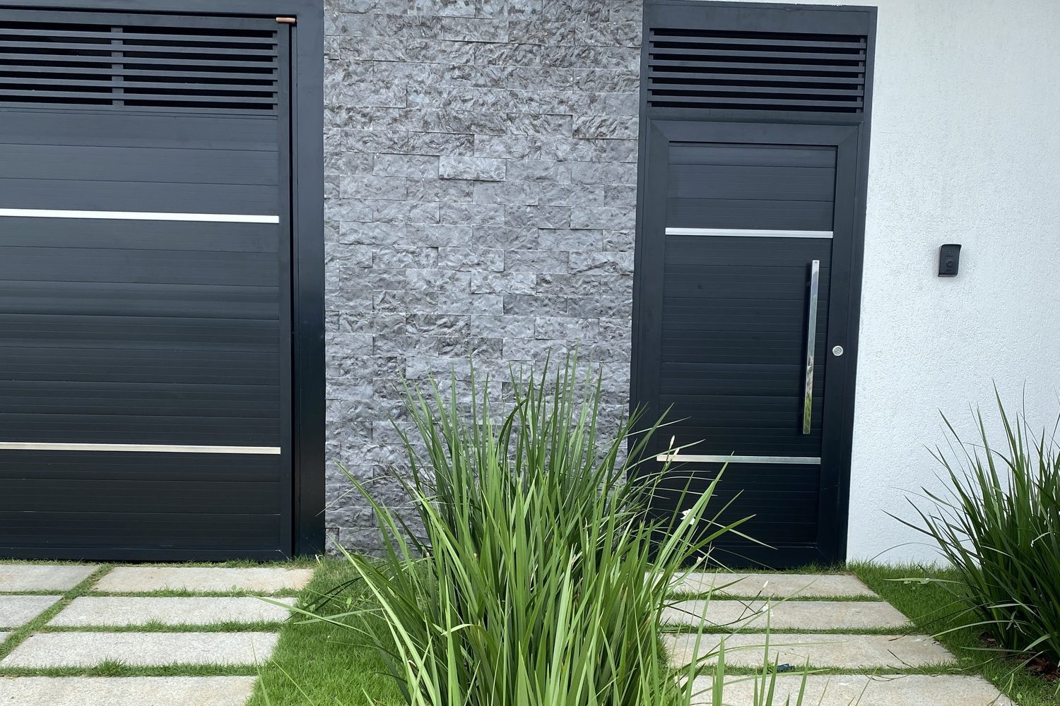Entrada de casa com faixa de rock face Matrix cinza entre o portão de garagem e a porta social, ambos em alumínio preto