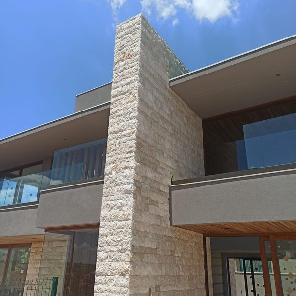 Torre da fachada de um sobrado revestida em rock face de travertino romano mix, com guarda-corpo de vidro