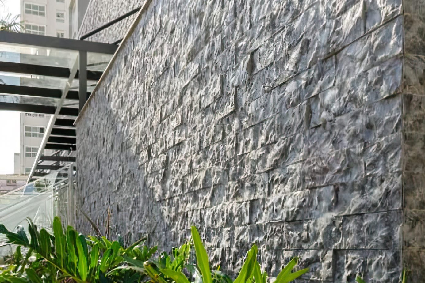 Muro alto revestido em Rock Face Matrix ao lado de um jardim
